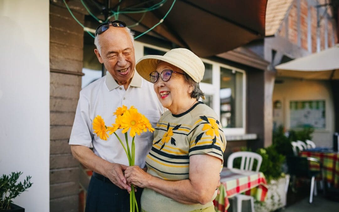 An older couple walks outside a cafe with a bouquet of bright yellow flowers.